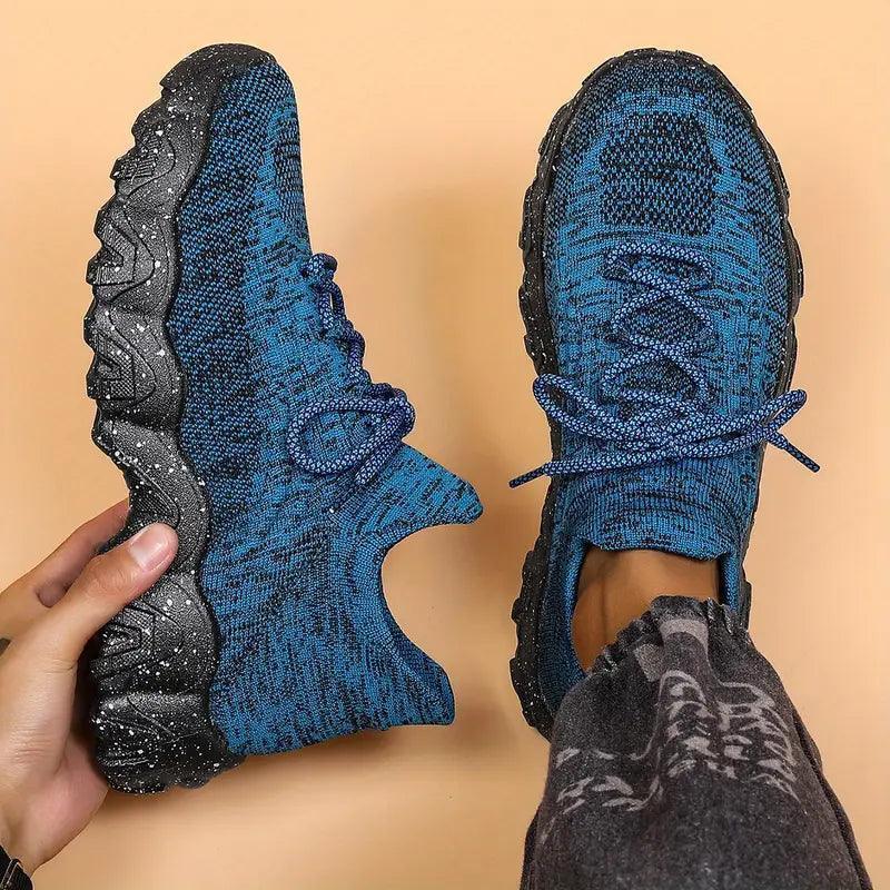 Top-down view of blue marled knit lace-up sneakers with black speckled soles, one held in hand and one worn with gray pants. 28