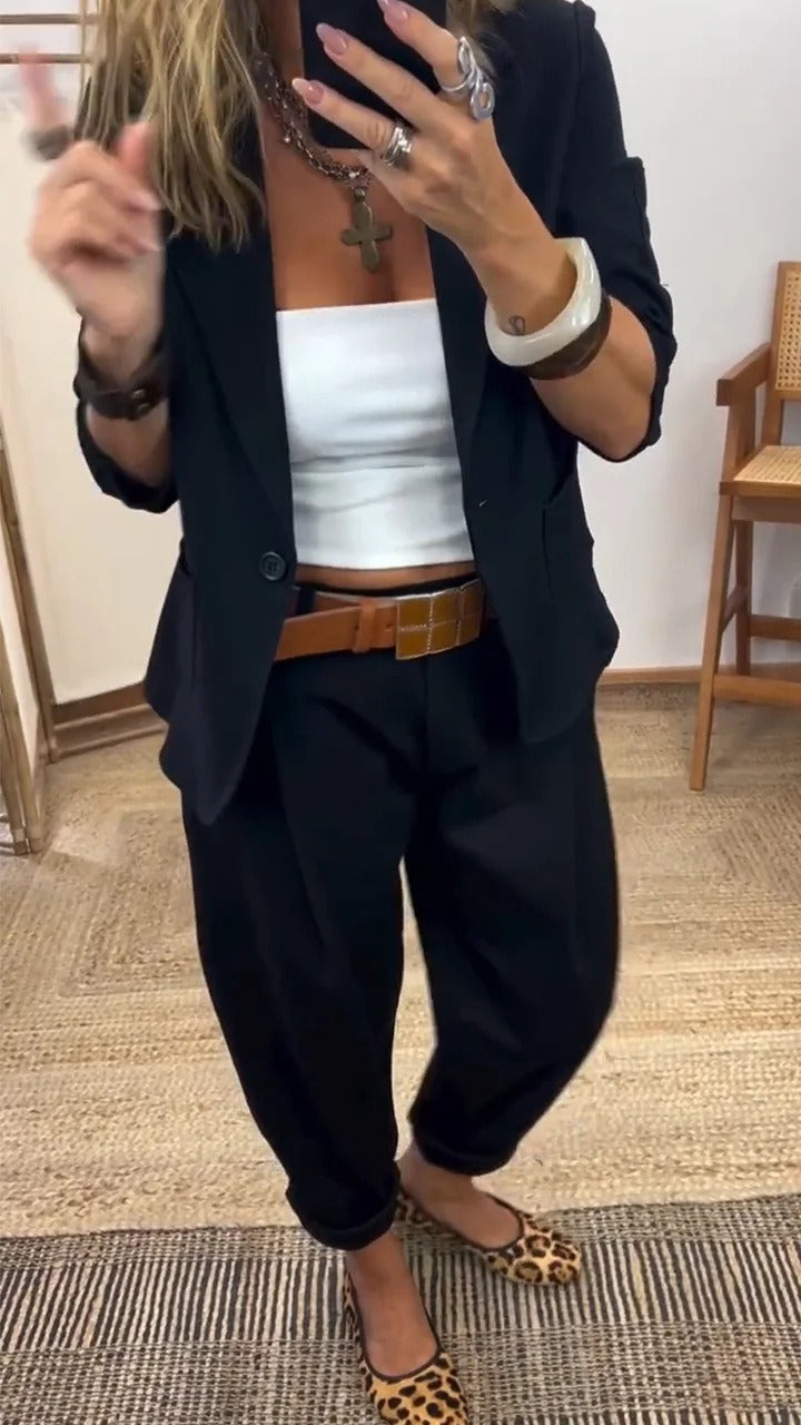 Black suit set with a one-button blazer and pleated pants, styled with a white top and tan belt.