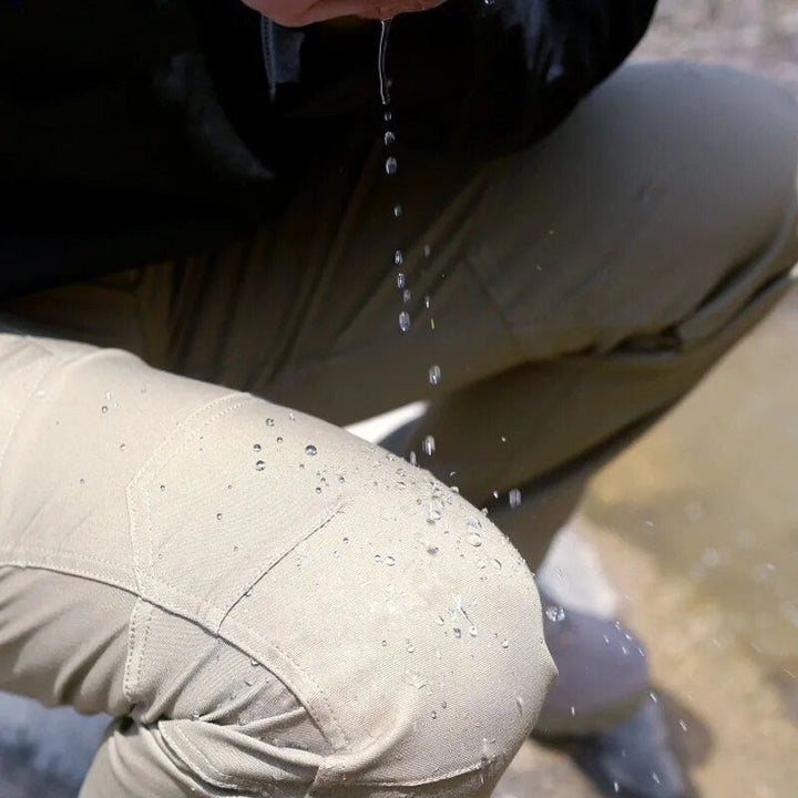 Men's khaki cargo pants close-up at the knee with water beading on the surface.