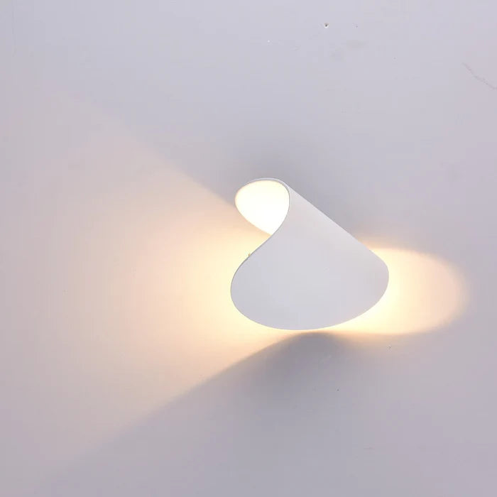 White wall light rotated at an angle, sending warm light out in two opposite directions across a pale wall.