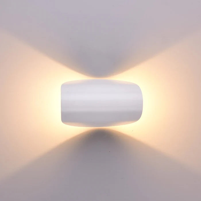 Front view of the white wall light set horizontally, glowing with warm light above and below on a pale wall.