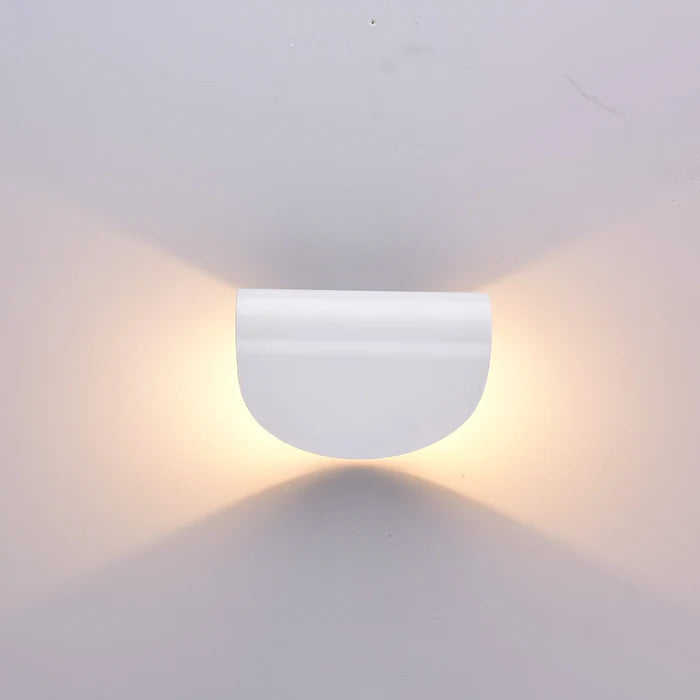 Front view of the white half-round wall light on a pale wall, warm light spreading above and below its flat edge.