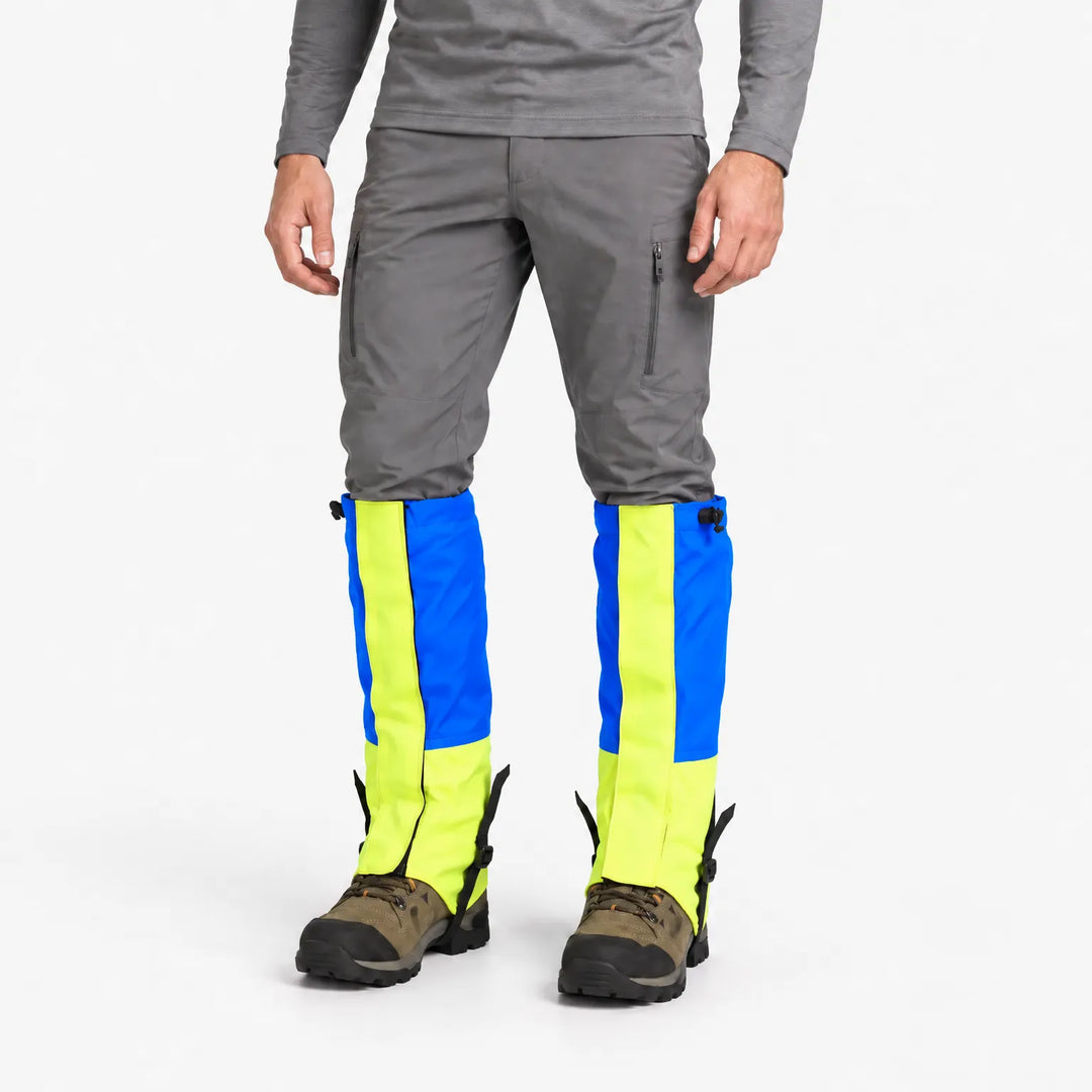 Man wearing blue and neon yellow gaiters over gray pants and hiking boots, shown in a three-quarter studio view. 2