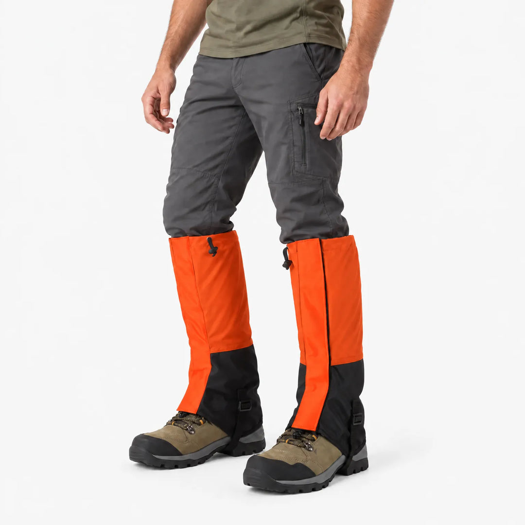Man in orange and black gaiters over dark gray pants and hiking boots, angled side view on white background. 4