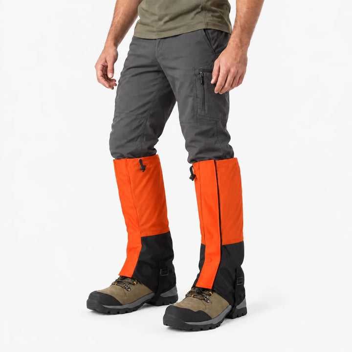 Man in orange and black gaiters over dark gray pants and hiking boots, angled side view on white background. 4