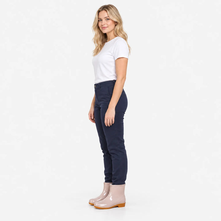 Woman in white t-shirt and navy pants stands in profile wearing pale pink glossy ankle rain boots with tan soles. 4