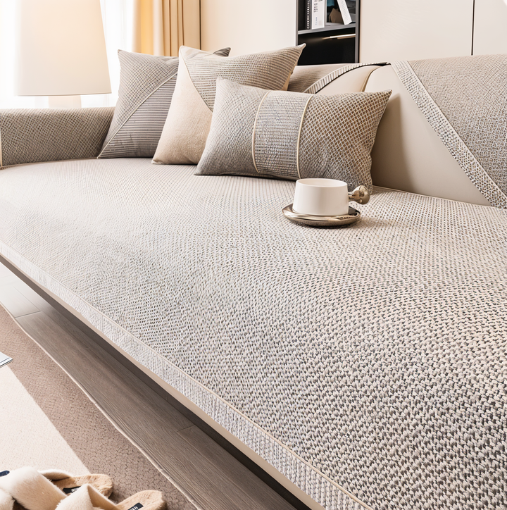 Beige-gray woven cover on a sofa seat with matching pillows, a white cup on a saucer, and slippers nearby. 1