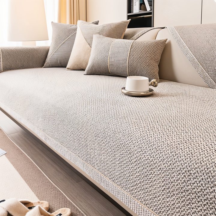 Beige-gray cover smoothly fitted over a sofa seat and backrest, with a cup on the seat and matching pillows. 5