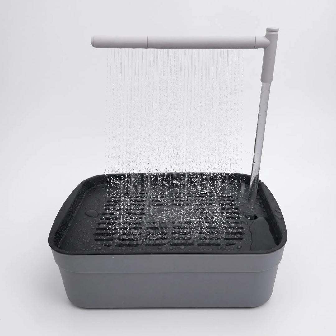 Gray bird bath with a dark slotted grate, a rain-style spray bar showering water down, and a vertical tube feeding it, on a white background. 1