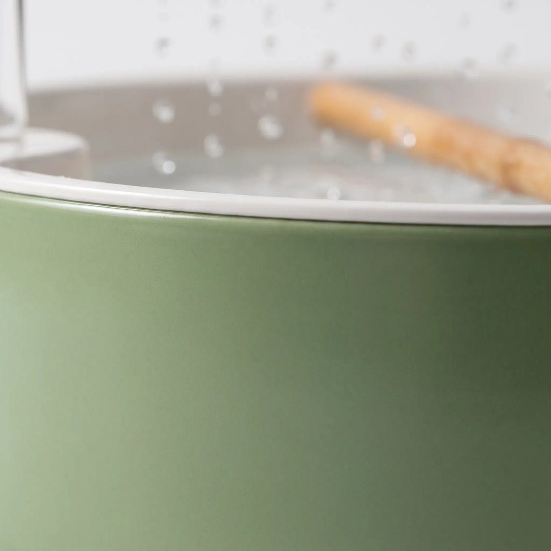 Close-up of the matte green outer wall and white rim of the bath, with the wooden perch and water droplets blurred behind. 4