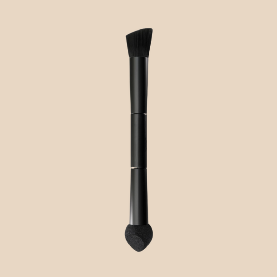 Black double-ended brush shown upright on a beige background, with an angled bristle head at the top and a small teardrop-shaped sponge tip at the bottom.
