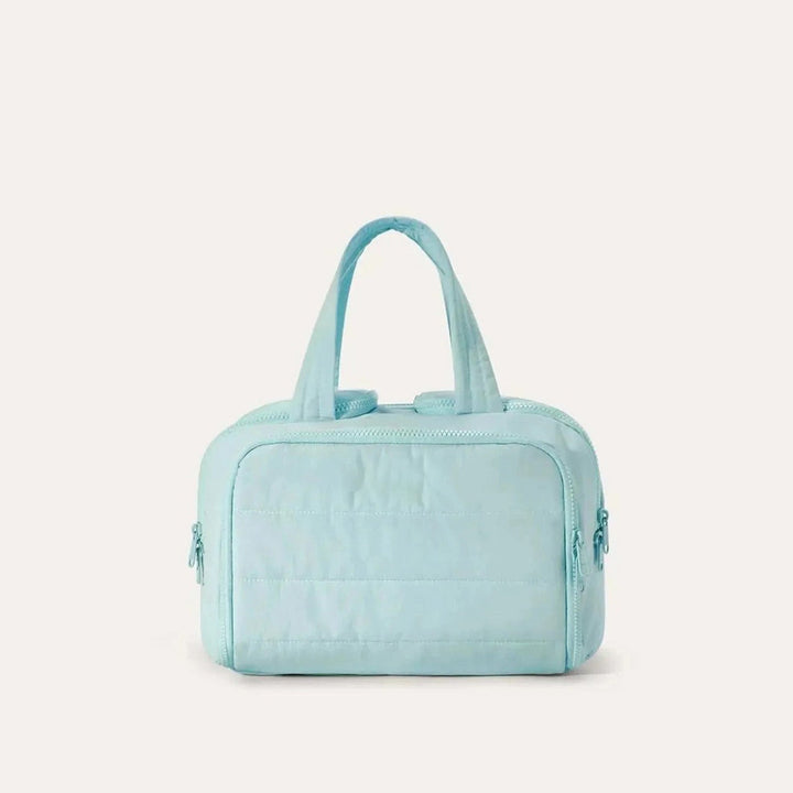 Quilted toiletry bag in light aqua blue, front view, with two top handles and zipper pulls on both sides. 15