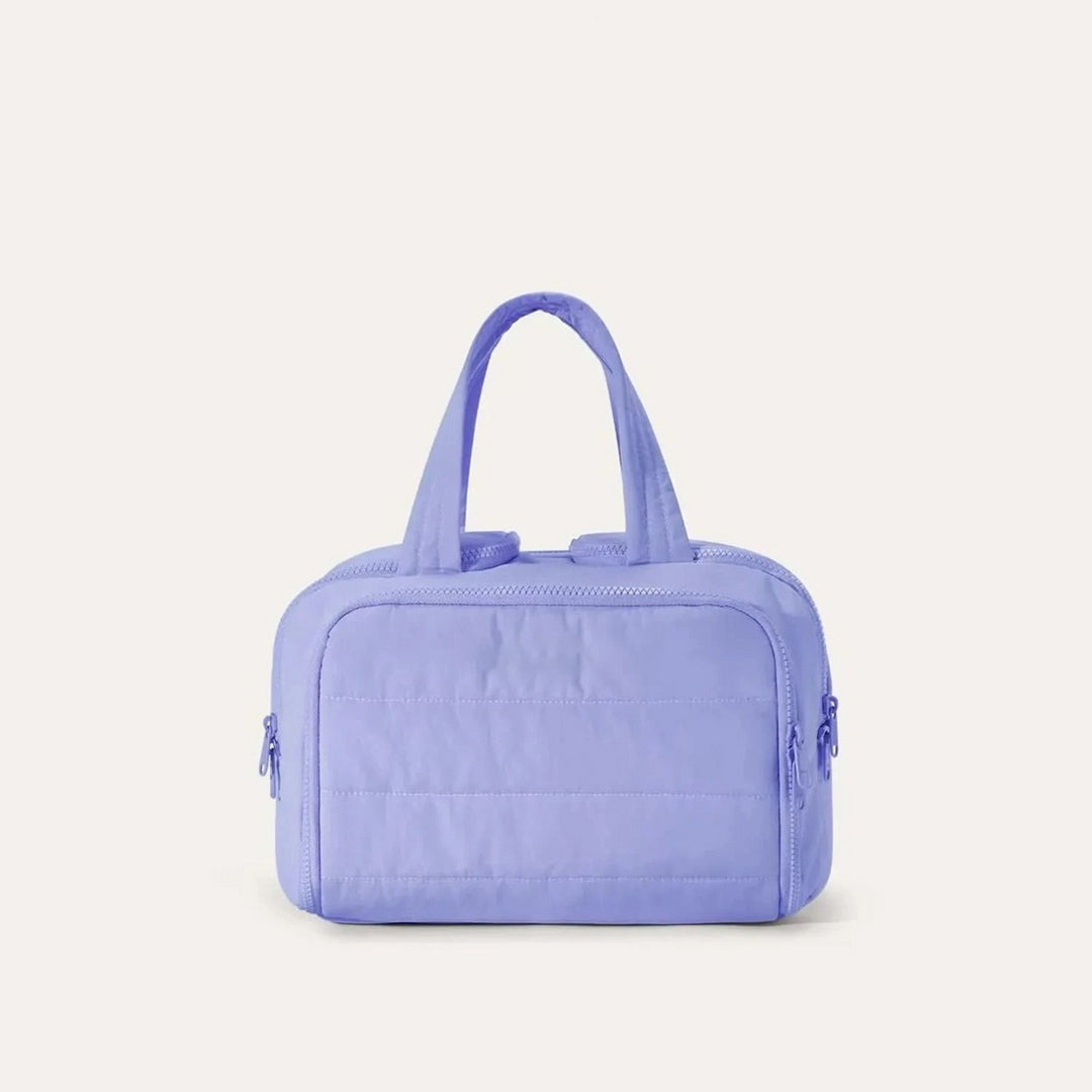 Quilted toiletry bag in periwinkle blue, front view, with two top handles and zipper pulls on both sides. 13