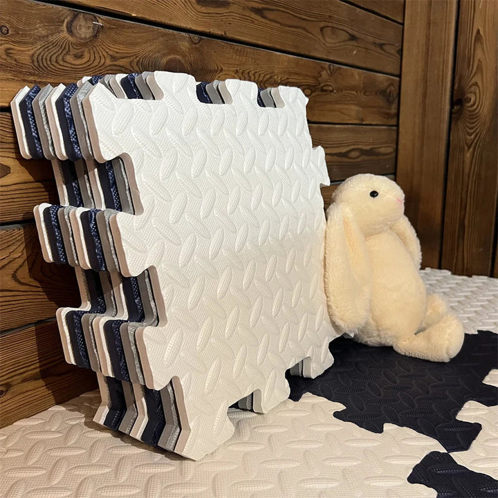 Stack of cream, gray and navy foam puzzle tiles beside a plush bunny on a laid mat.