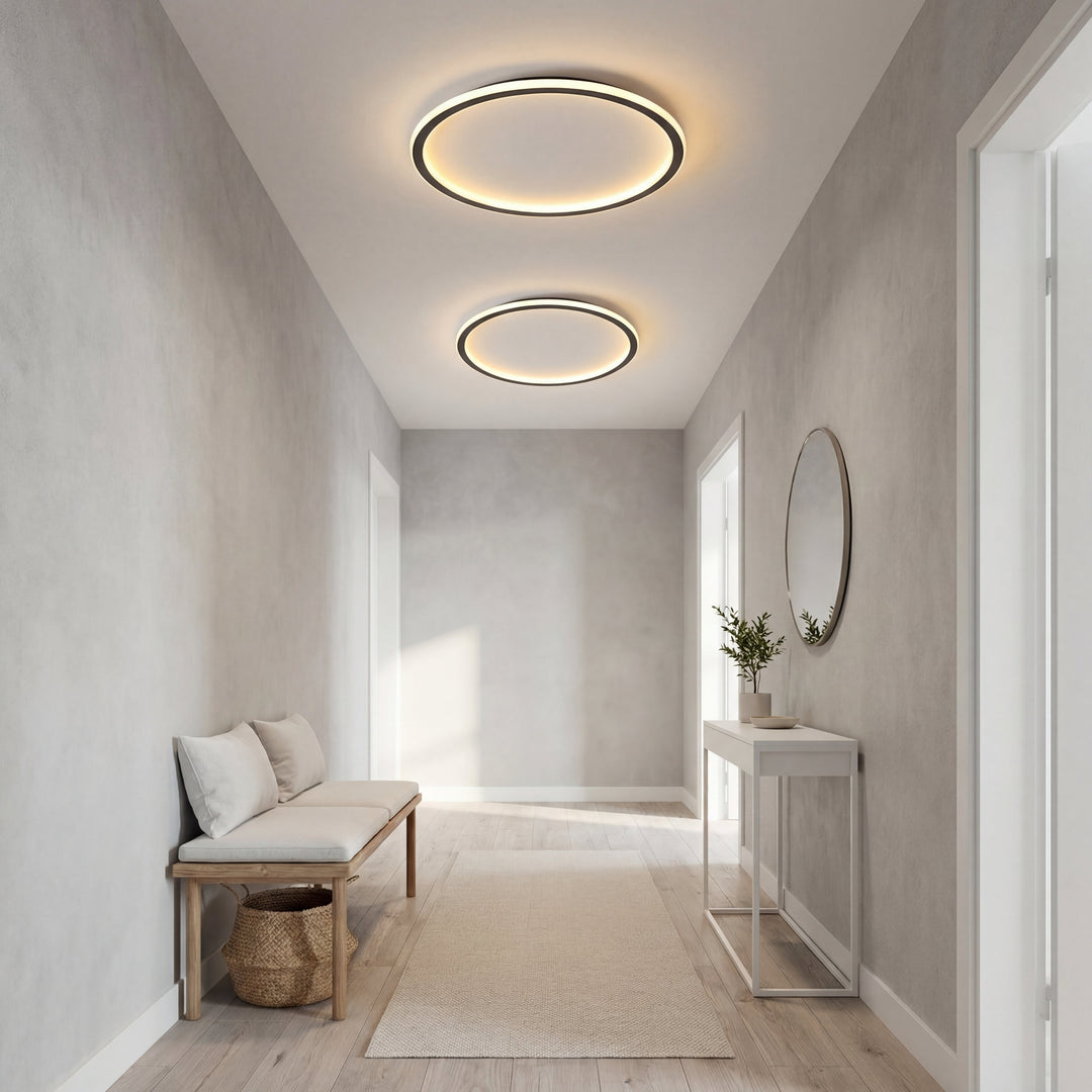 Two ring ceiling lights in different sizes lit in a long entryway with a bench, console table and round mirror. 6
