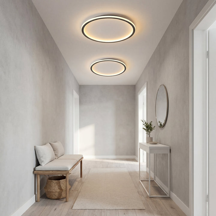 Two ring ceiling lights in different sizes lit in a long entryway with a bench, console table and round mirror. 6
