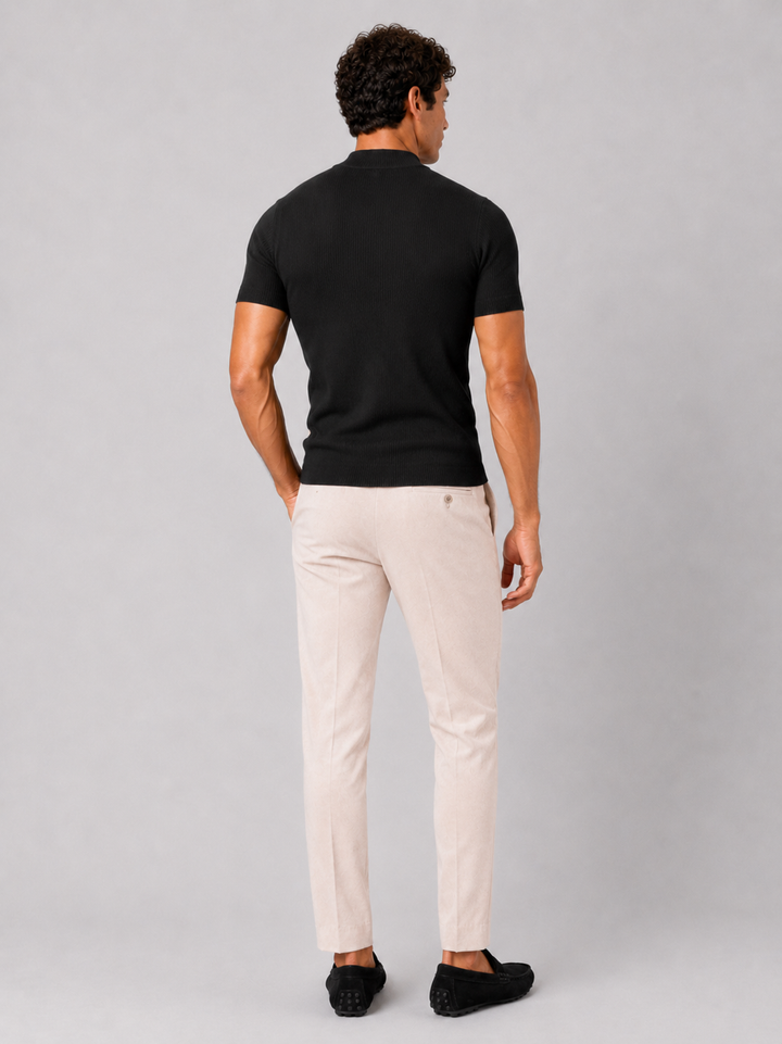 Back view of the men's black ribbed mock neck tee with cream trousers and black loafers.
