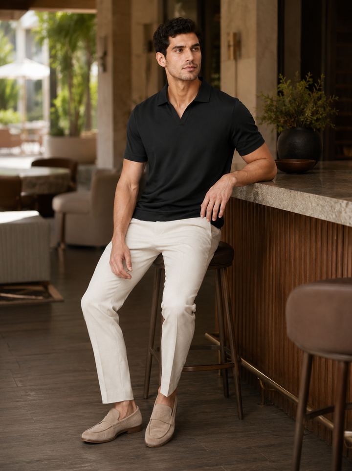 Black silky touch polo shirt styled with cream trousers on a model.