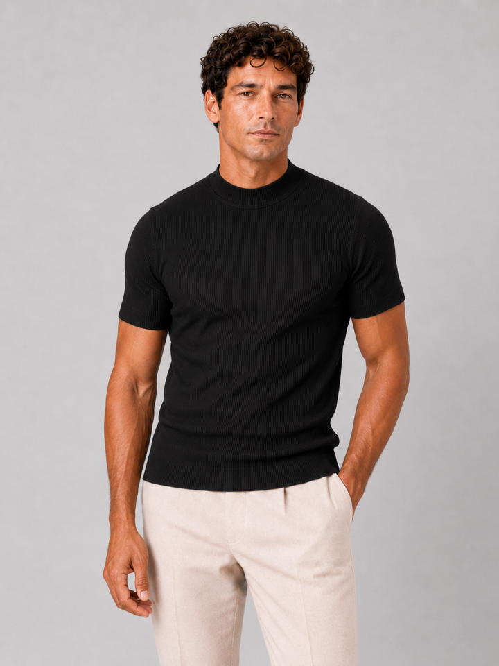 Front view of a men's black ribbed mock neck tee with cream trousers, hand in pocket.