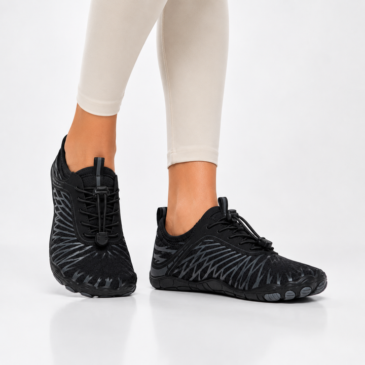Woman in cream leggings wearing the black and gray barefoot shoes, front view against a plain light background.