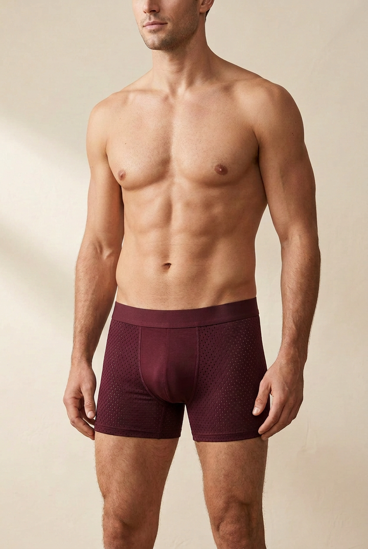 Shirtless male model wearing burgundy boxer briefs with perforated mesh side panels and a smooth center pouch 1