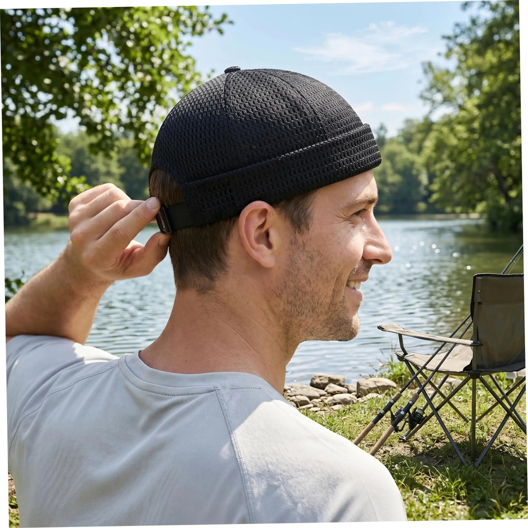 Man in a gray tee by a lake, adjusting the strap on a black open weave brimless cap 1