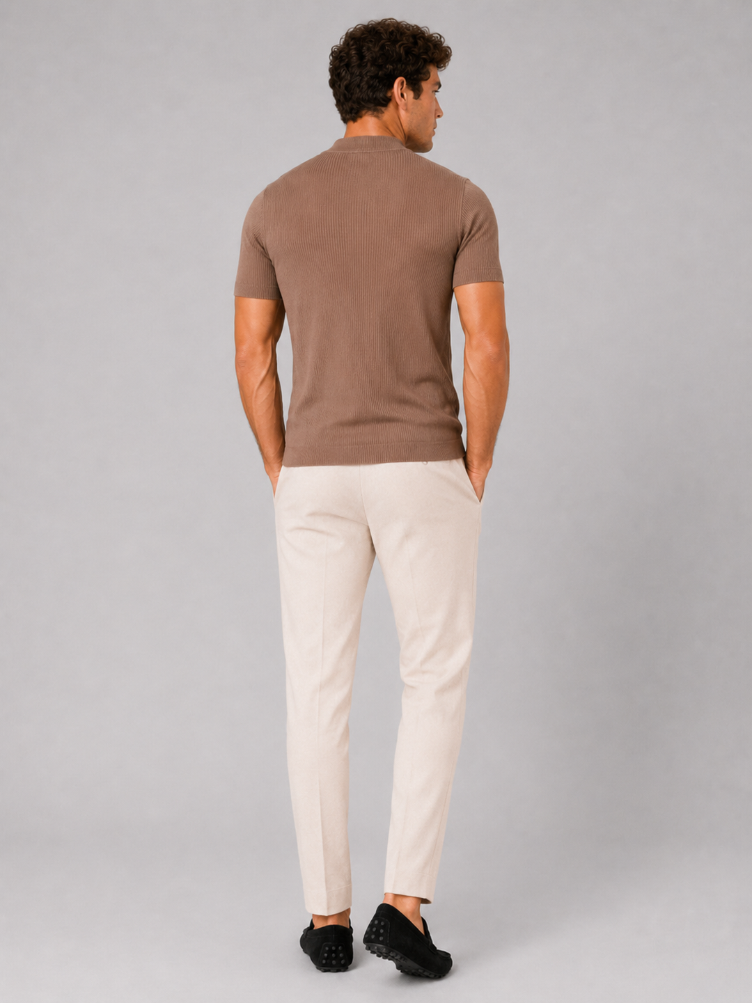 Back view of the men's brown ribbed mock neck tee with cream trousers and black loafers.