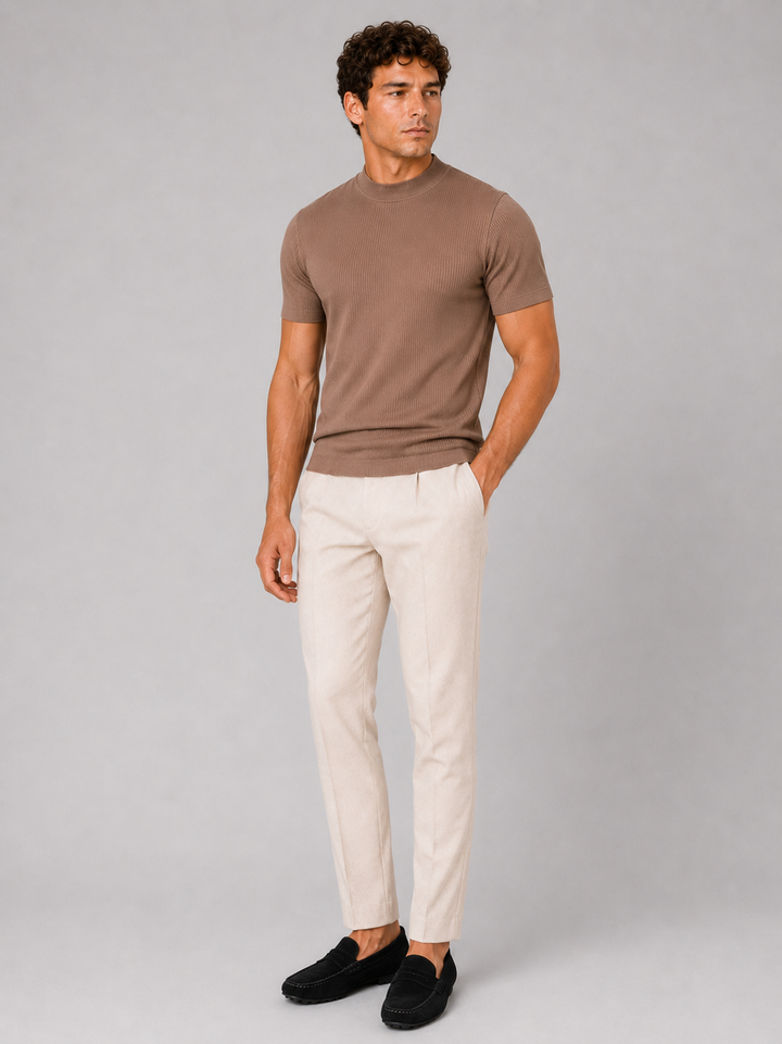 Men's brown ribbed tee worn tucked-out with cream pleated trousers and black suede loafers.