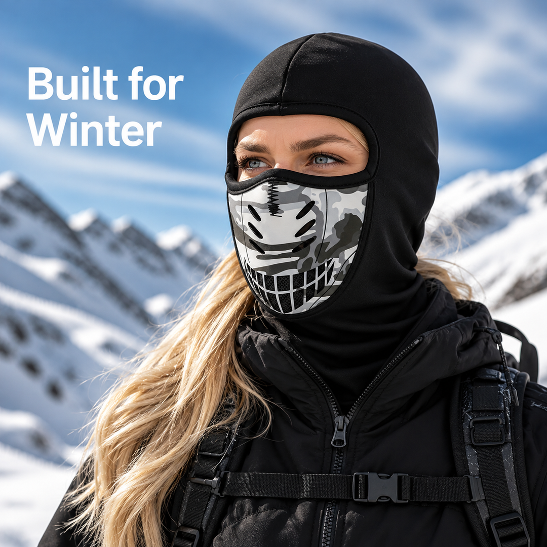 Woman in a black balaclava with a gray camo vented mouth panel, standing before snowy mountains 1