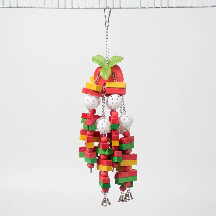 Hanging parrot toy with red apple-shaped top and green leaves, colored wooden blocks, white perforated balls and small bells, hooked to a cage roof. 1