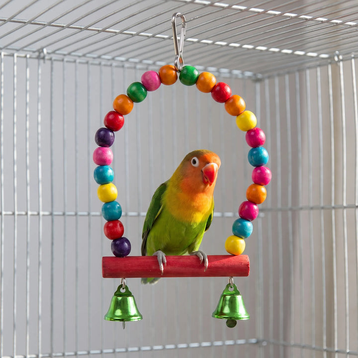 Lovebird perched on the red wooden bar of a colorful bead arch swing with two green bells inside a cage. 2