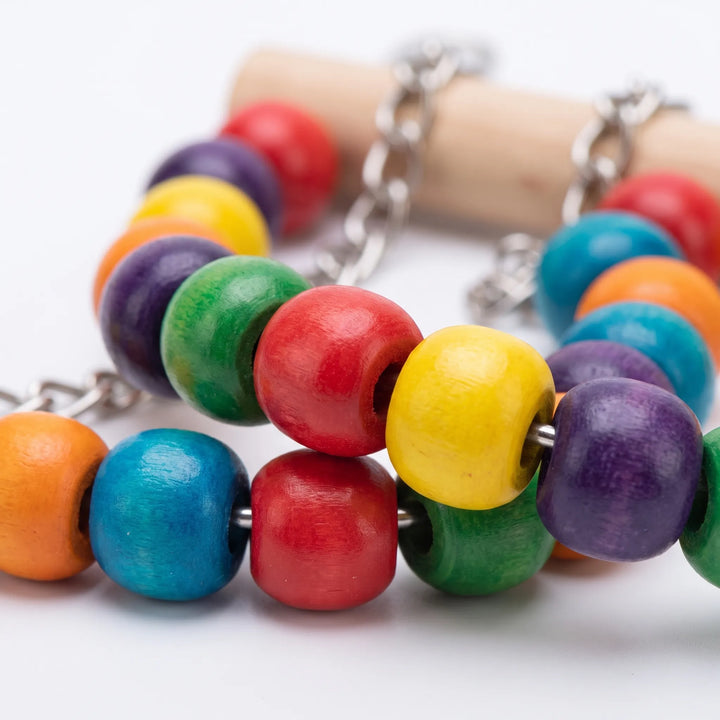 Close-up of glossy wooden beads in rainbow colors threaded on metal wire, with a natural wood perch and chain behind. 4