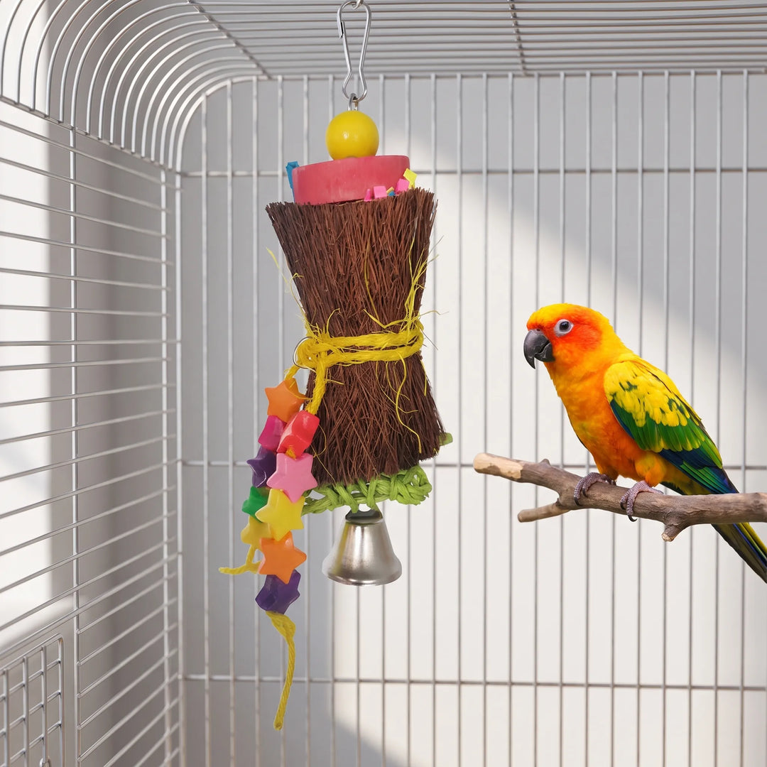 Fiber shredding toy with pink block, yellow bead, star-bead strand and bell hanging inside a cage next to a sun conure. 4