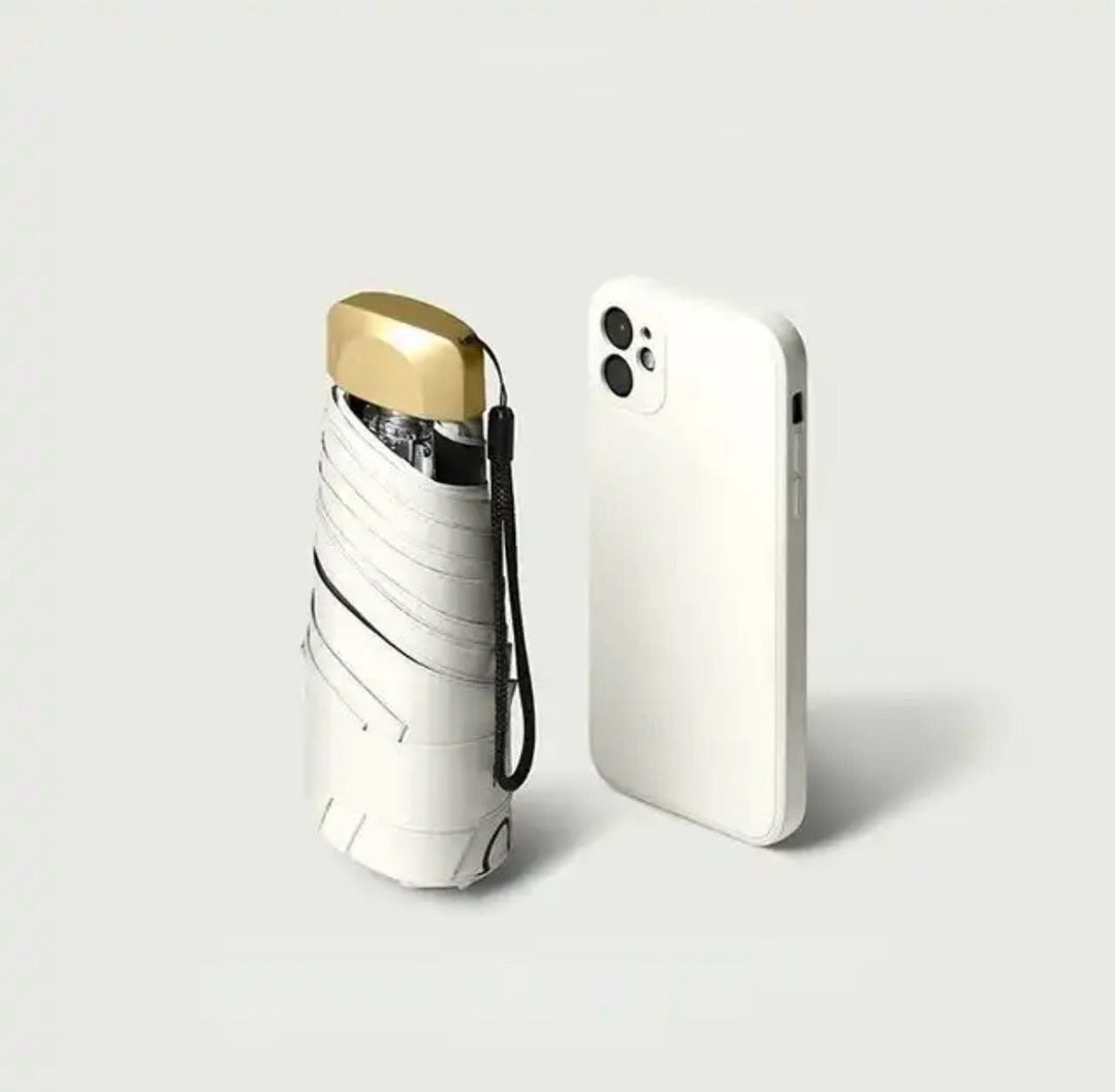 Folded white umbrella with a gold cap and wrist strap next to a white smartphone on a light gray background.