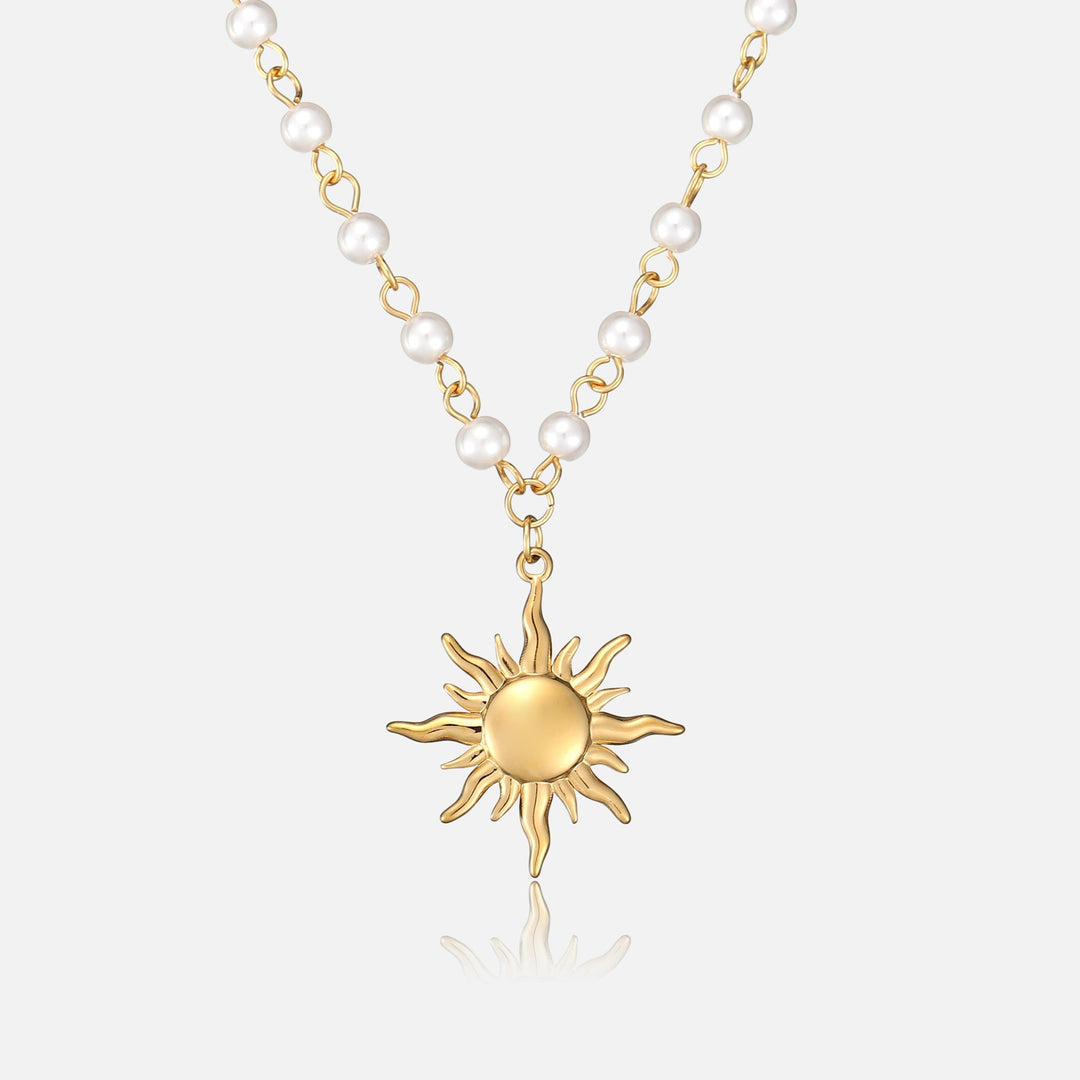 Front view of a gold sun pendant hanging from a chain of round white pearls 1