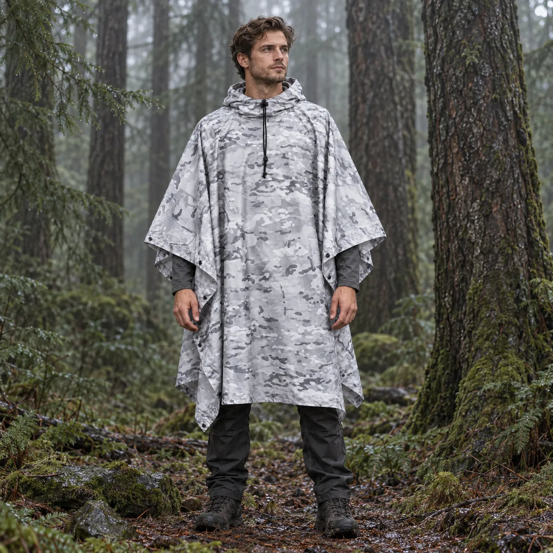 Man standing in a misty evergreen forest wearing a hooded poncho in white and gray camouflage with a black drawcord. 3
