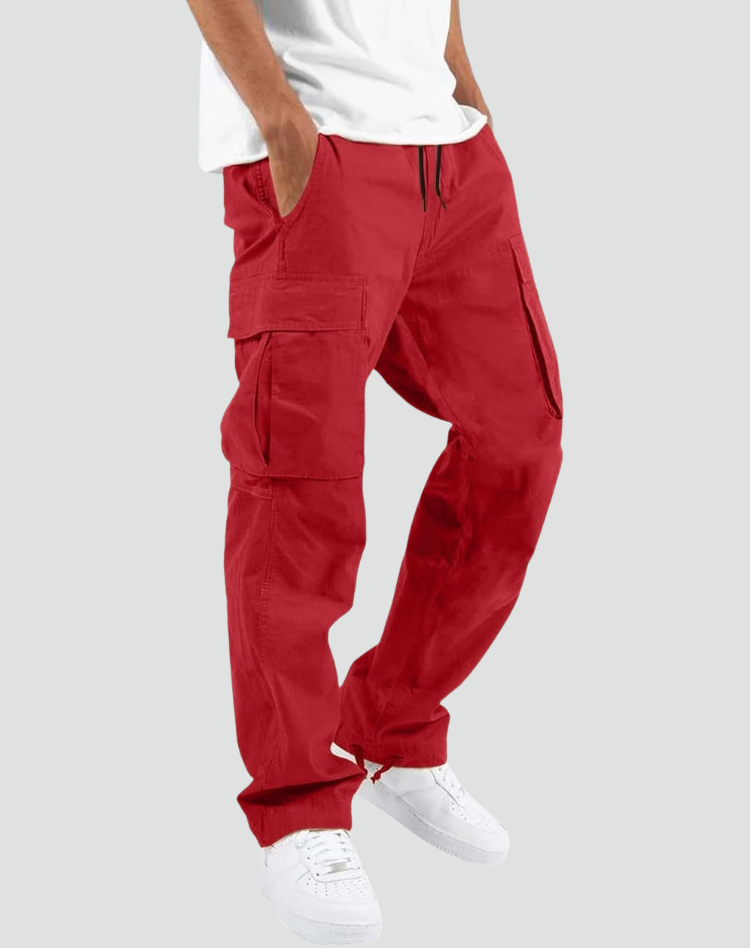 Model wearing red cargo pants with white tee and white sneakers, hand in pocket, side view on gray. 10