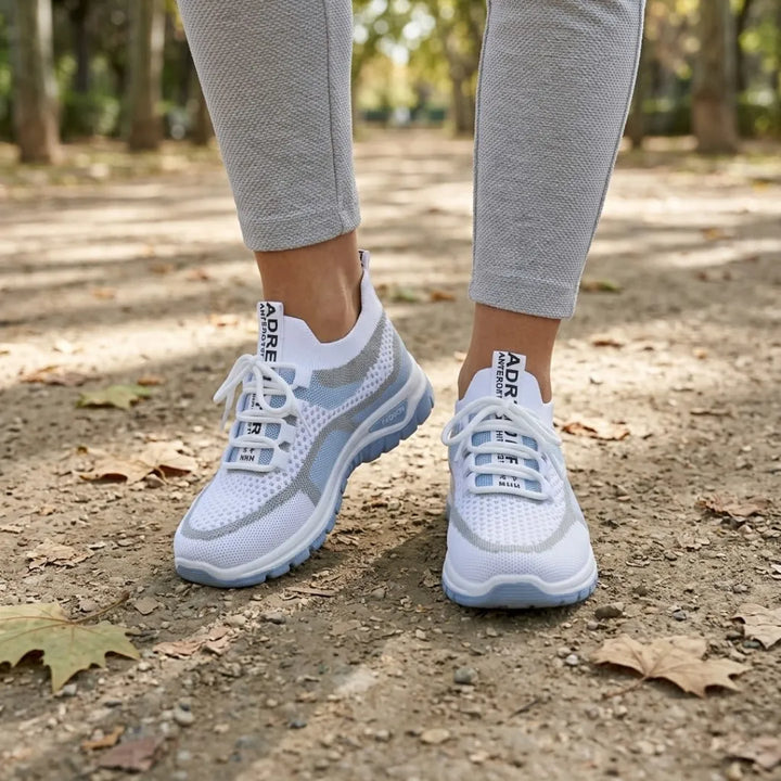 Pair of white and light blue mesh sneakers worn by a woman in gray leggings on a leafy park path. 2