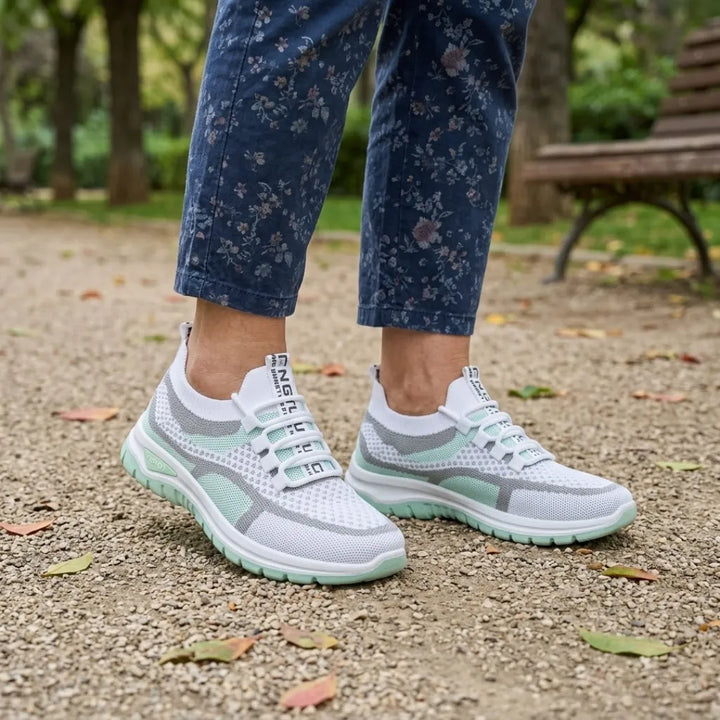 Pair of white and mint green mesh sneakers worn with floral blue cropped pants on a gravel park path near a bench. 11
