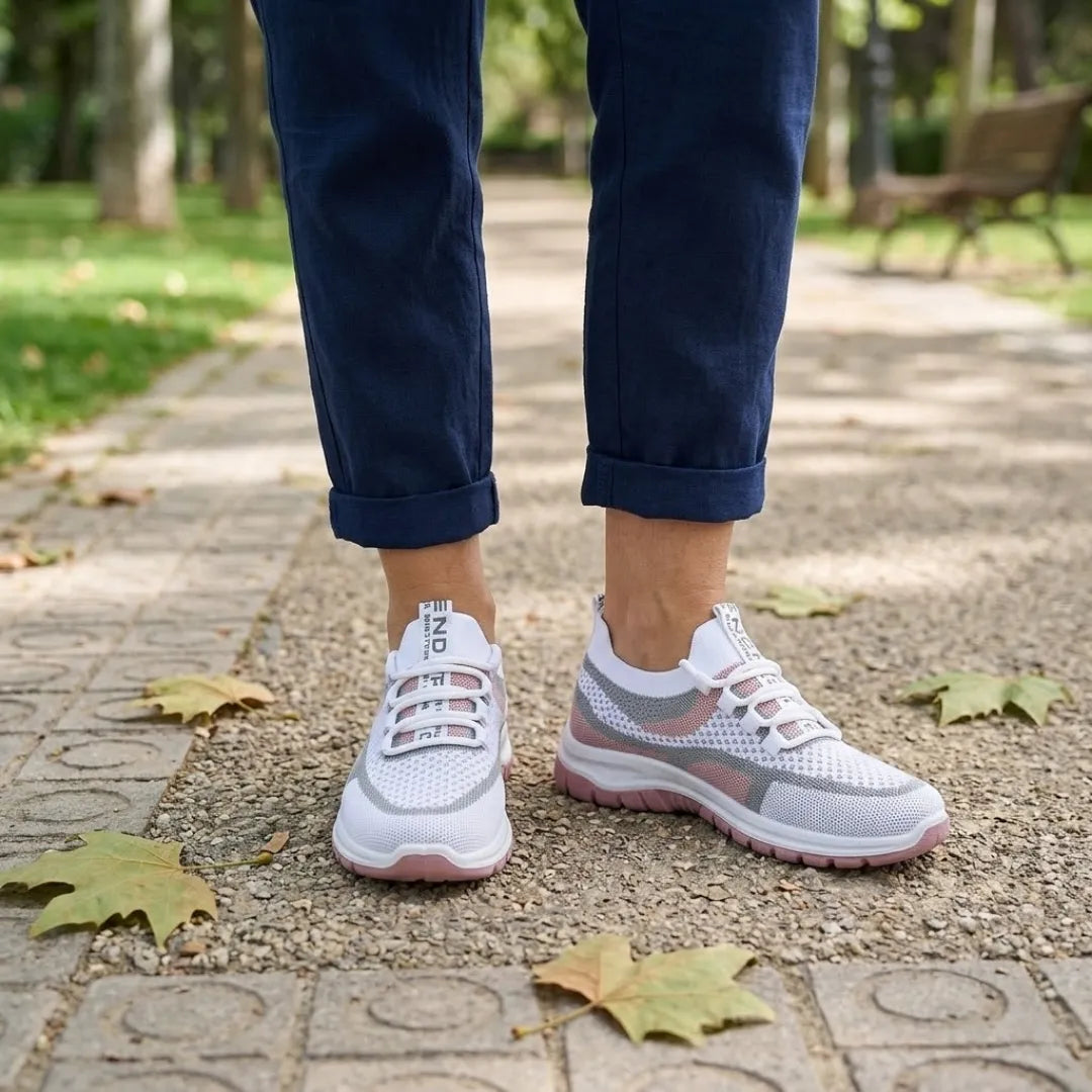 Pair of white and pink mesh sneakers worn with rolled navy pants on a paved park path with fallen leaves. 20
