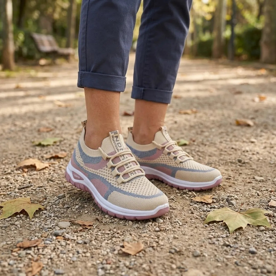 Woman wearing beige mesh knit sneakers with pink and blue stripes and white soles, standing on a gravel park path with fallen leaves. 29