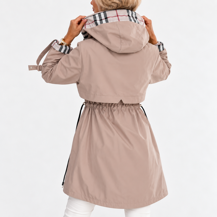 Back view of the beige coat showing the hood raised by both hands and the gathered drawstring waist 3
