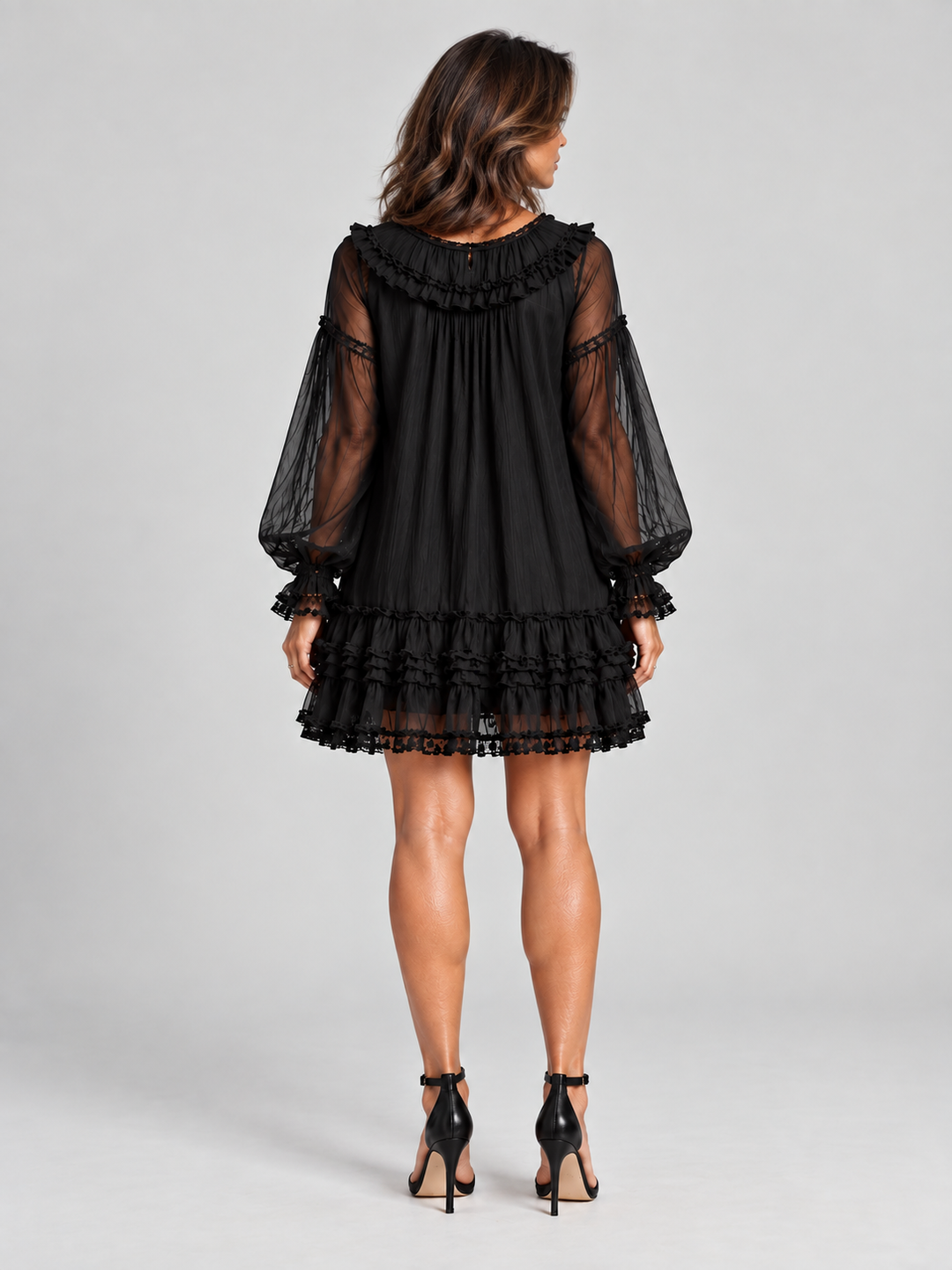 Back view of the black dress on a model, showing the ruffled collar, gathered fabric, sheer sleeves and lace-trimmed tiered hem. 4