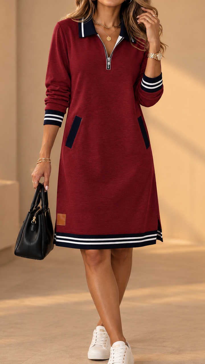 Burgundy red long-sleeve zip-neck dress with navy collar, pocket trim and striped hem, worn with white sneakers and a black handbag.