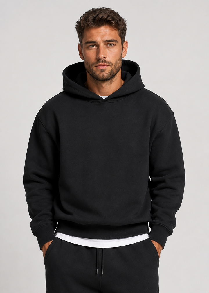 Men's black hoodie detail, front view with ribbed cuffs and hem over a white tee.