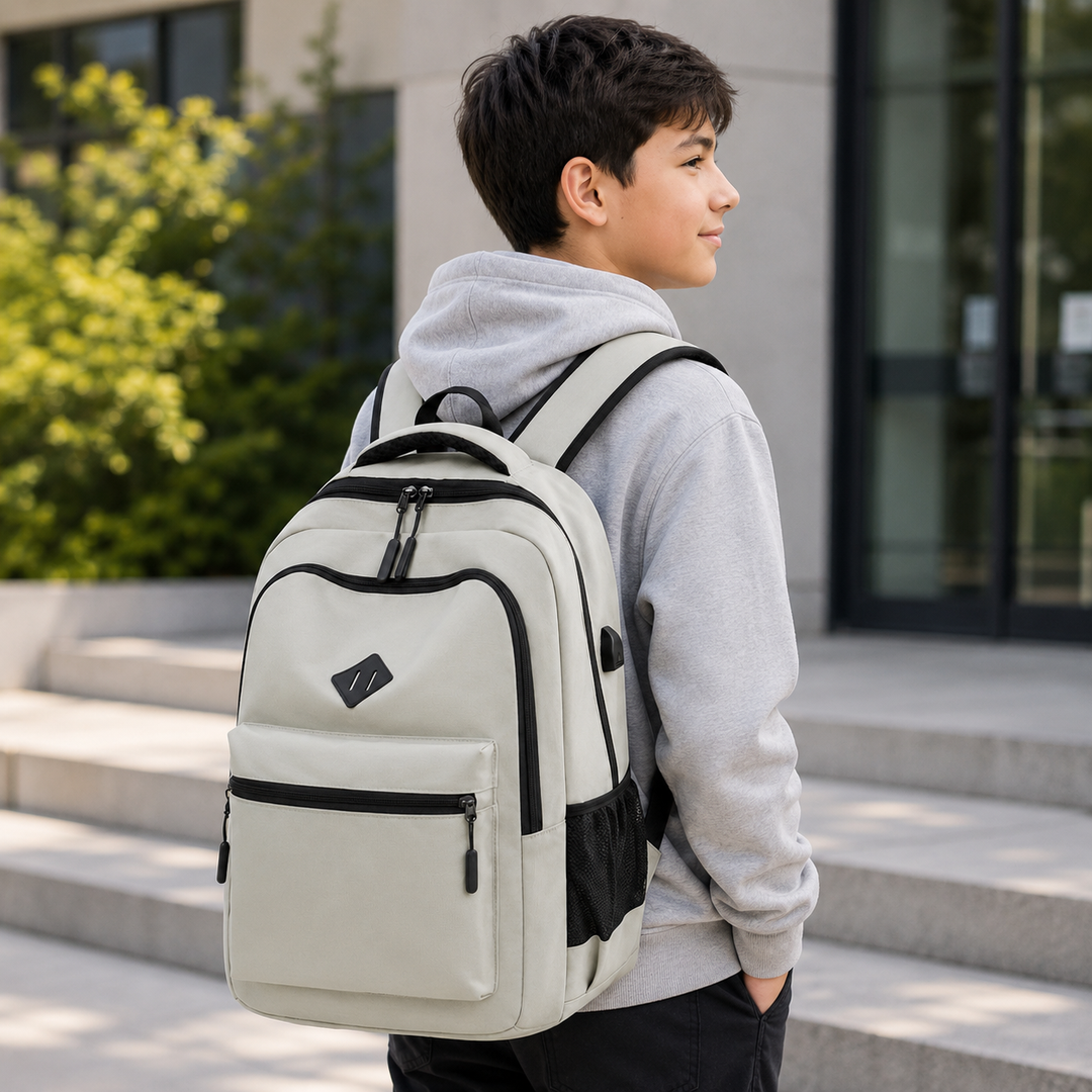 Teenage boy in a gray hoodie wearing the black backpack on his shoulders while standing on steps outside a school building.