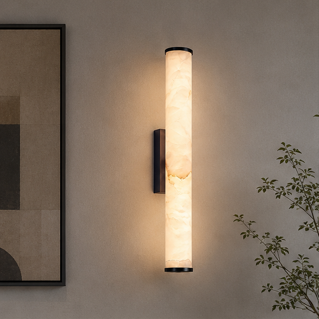 Black-finish marble cylinder sconce glowing on a taupe wall beside an abstract framed artwork and a leafy branch.