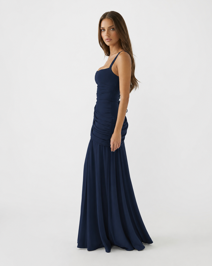 Side view of a navy blue maxi dress with ruched waist drape and a long flowing skirt