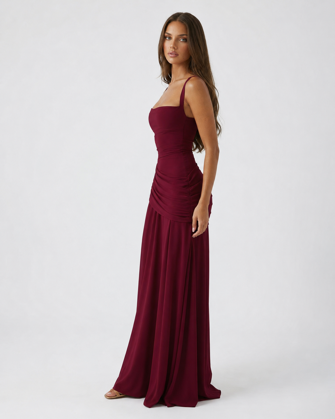 Side view of a burgundy maxi dress with fitted ruched waist and a long flowing skirt