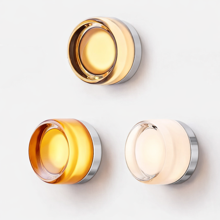 another view of three round glass wall lights with chrome backplates in amber, deeper orange and soft white.
